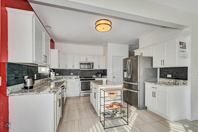 kitchen featuring appliances with stainless steel finishes, a sink, light stone counters, and white cabinets