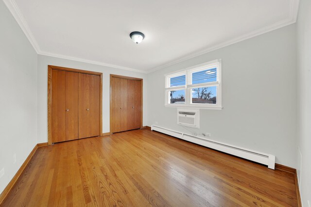 unfurnished bedroom with a baseboard heating unit, light hardwood / wood-style flooring, ornamental molding, a wall mounted AC, and multiple closets