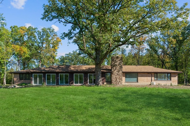 back of house with a yard, brick siding, and a chimney