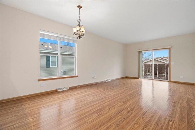 empty room with a notable chandelier and light hardwood / wood-style floors