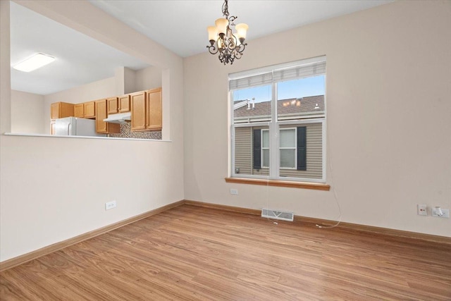 unfurnished room with light wood-type flooring and an inviting chandelier