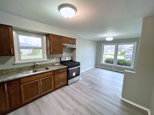 kitchen featuring stainless steel gas range oven, light stone countertops, sink, and light hardwood / wood-style flooring