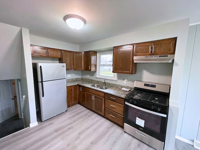 kitchen featuring sink, light stone counters, stainless steel range oven, light hardwood / wood-style floors, and fridge