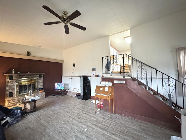 living room with hardwood / wood-style floors, ceiling fan, and a stone fireplace