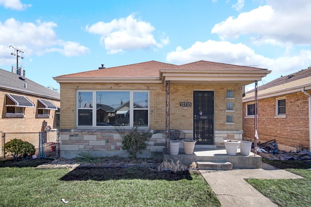 bungalow featuring brick siding, covered porch, a front lawn, and fence