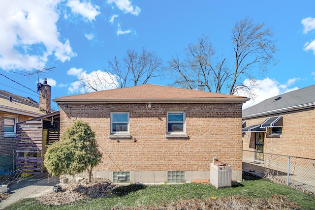 back of house featuring brick siding, central AC unit, roof with shingles, and fence