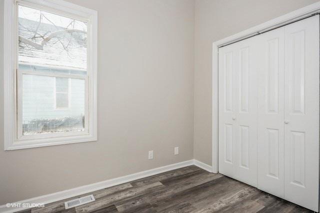 unfurnished bedroom with multiple windows, dark hardwood / wood-style flooring, and a closet