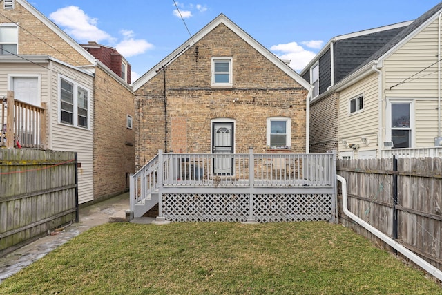 back of property with a deck, brick siding, a lawn, and fence