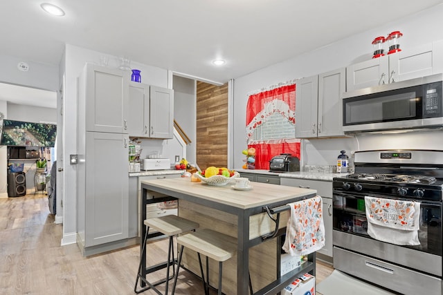 kitchen with light wood-style flooring, gray cabinetry, recessed lighting, stainless steel appliances, and wooden walls