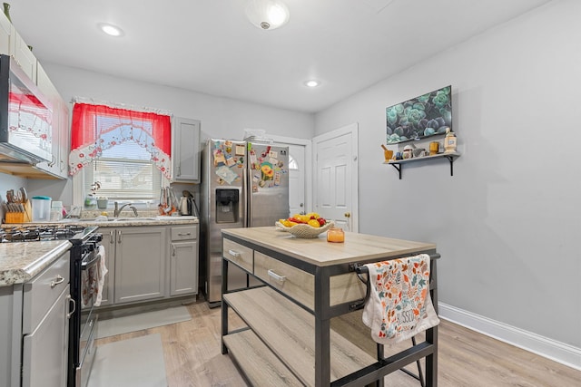 kitchen featuring baseboards, appliances with stainless steel finishes, gray cabinets, light wood-style floors, and a sink