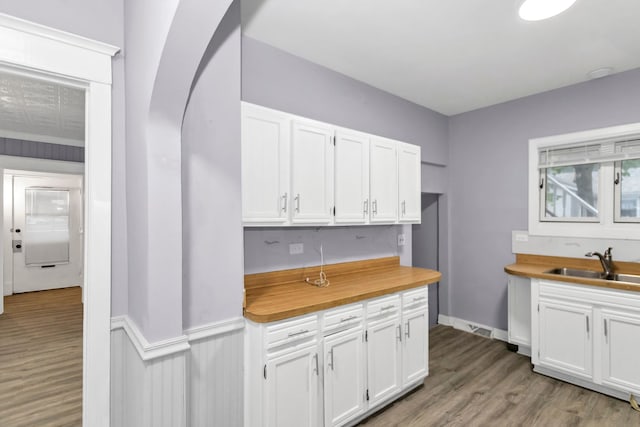kitchen featuring wood finished floors, butcher block countertops, white cabinetry, arched walkways, and a sink