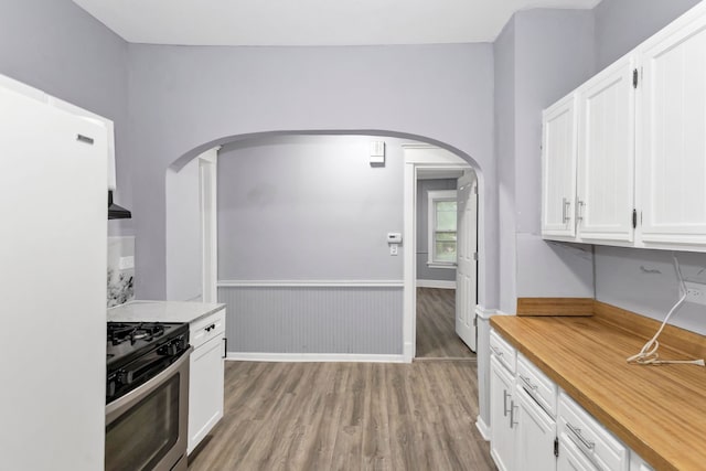 kitchen with arched walkways, stainless steel gas stove, wood finished floors, freestanding refrigerator, and white cabinetry