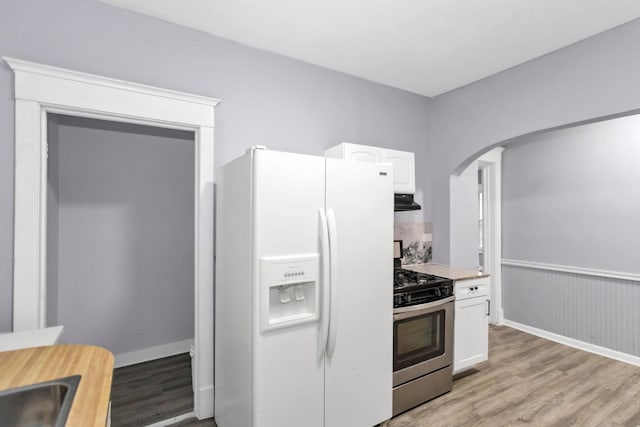 kitchen with light wood finished floors, arched walkways, white fridge with ice dispenser, stainless steel range with gas cooktop, and white cabinetry