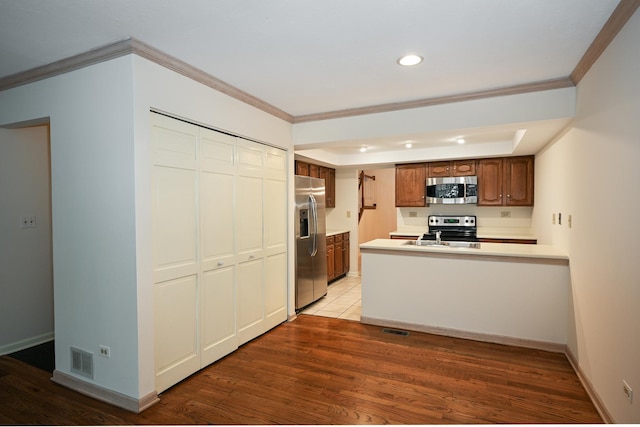 kitchen featuring ornamental molding, appliances with stainless steel finishes, light wood-type flooring, and kitchen peninsula