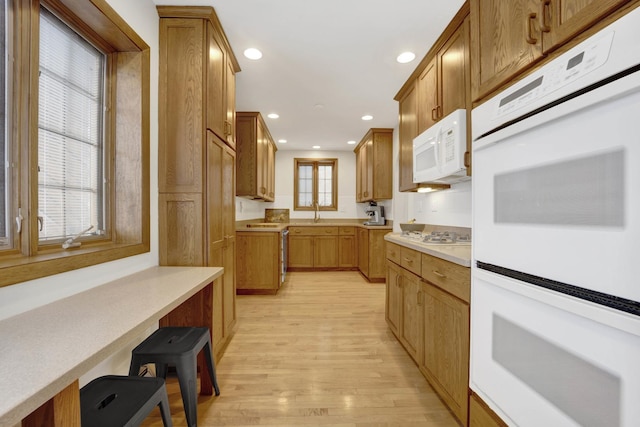 kitchen featuring white appliances, light hardwood / wood-style floors, a breakfast bar, and sink