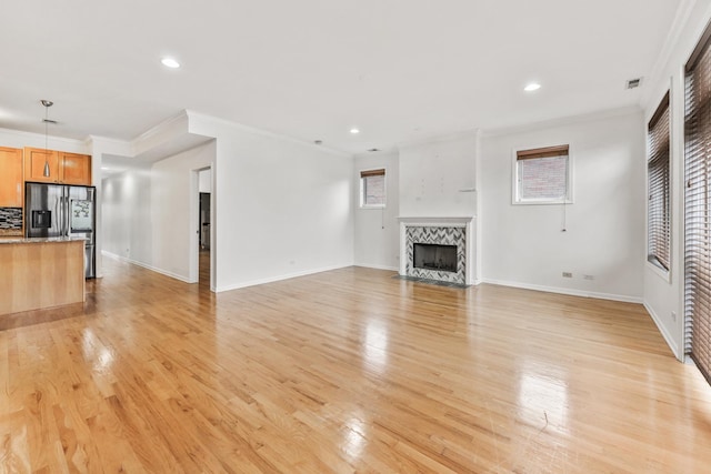 unfurnished living room with a tiled fireplace, crown molding, and light wood-type flooring