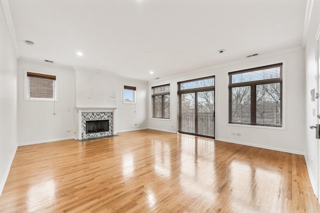 unfurnished living room featuring a tile fireplace, light hardwood / wood-style floors, a wealth of natural light, and ornamental molding