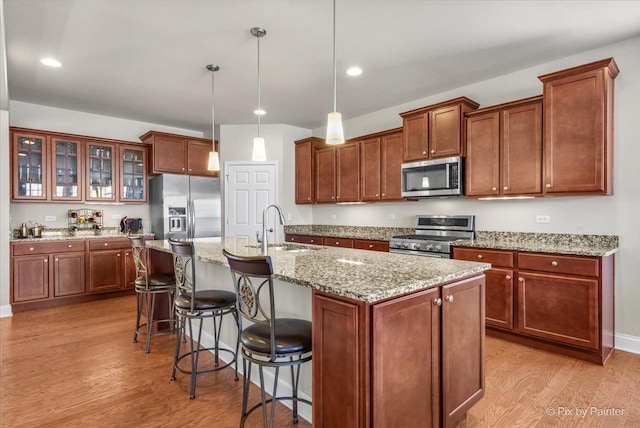 kitchen featuring sink, light hardwood / wood-style flooring, pendant lighting, a kitchen island with sink, and appliances with stainless steel finishes