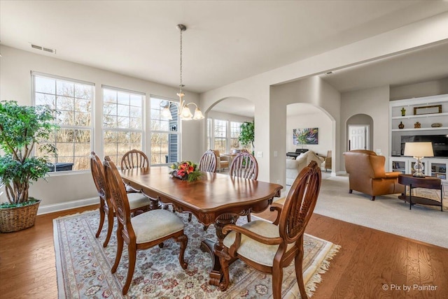 dining area with hardwood / wood-style floors, built in features, and an inviting chandelier