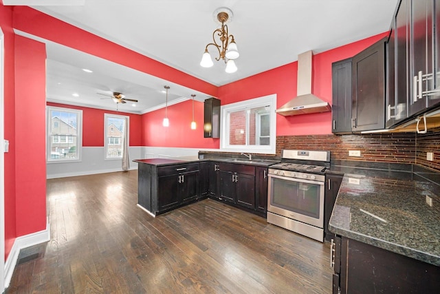 kitchen with stainless steel gas stove, dark wood finished floors, a peninsula, wall chimney range hood, and a sink