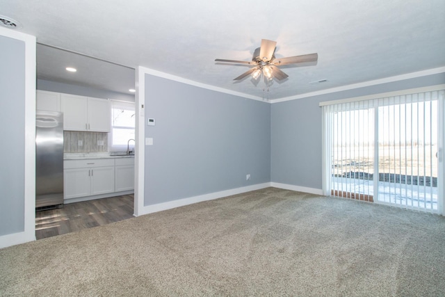 carpeted spare room with ceiling fan, plenty of natural light, sink, and crown molding