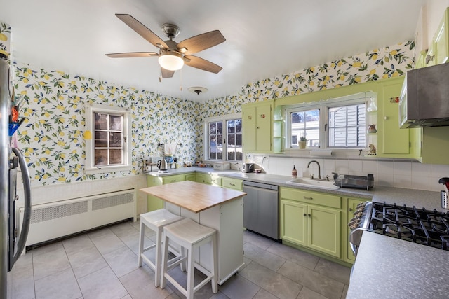 kitchen featuring radiator heating unit, green cabinets, sink, light tile patterned flooring, and stainless steel appliances