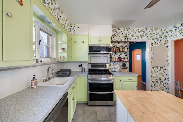 kitchen featuring light tile patterned floors, green cabinetry, sink, backsplash, and stainless steel appliances