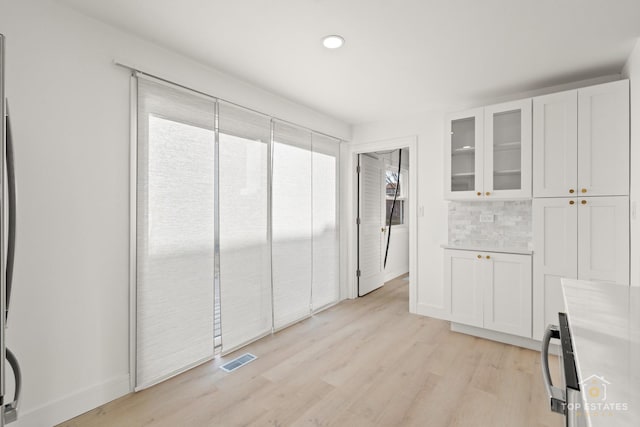 kitchen with light wood-type flooring, backsplash, and white cabinetry