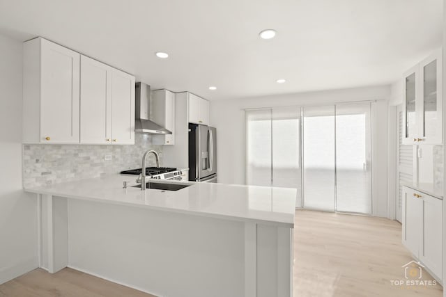 kitchen with wall chimney exhaust hood, stainless steel fridge, white cabinetry, and kitchen peninsula