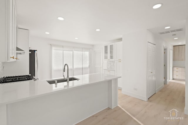 kitchen with kitchen peninsula, white cabinetry, sink, and ventilation hood