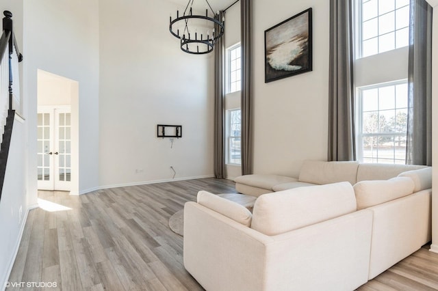 living room featuring an inviting chandelier, a towering ceiling, a healthy amount of sunlight, and light hardwood / wood-style floors