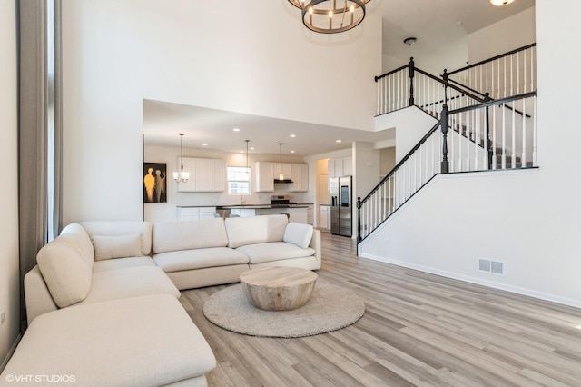 living room with an inviting chandelier, a high ceiling, and light wood-type flooring