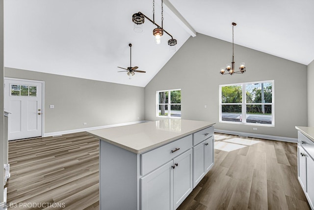 kitchen with white cabinetry, hanging light fixtures, light hardwood / wood-style flooring, a kitchen island, and ceiling fan with notable chandelier