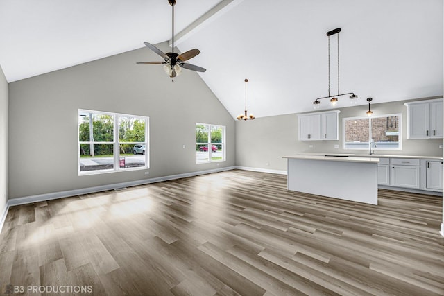 unfurnished living room featuring ceiling fan with notable chandelier, light hardwood / wood-style flooring, and high vaulted ceiling