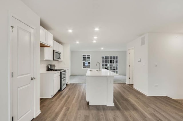 kitchen with a center island with sink, white cabinets, stainless steel appliances, and light wood-type flooring