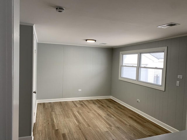 empty room with light hardwood / wood-style floors, crown molding, and wooden walls