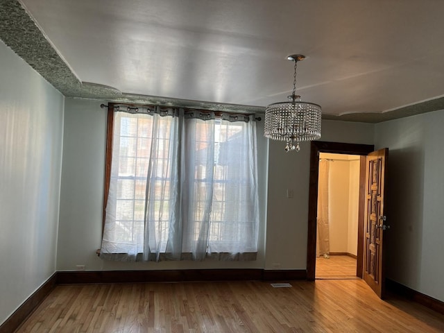 unfurnished dining area featuring an inviting chandelier and light hardwood / wood-style flooring