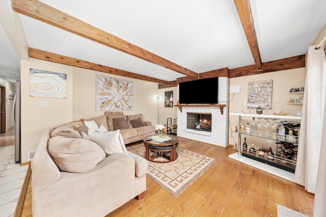 living room featuring beam ceiling, light hardwood / wood-style flooring, a brick fireplace, and bar