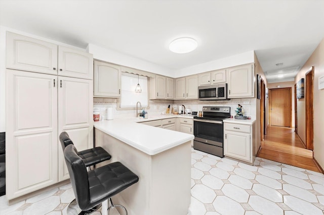 kitchen featuring backsplash, kitchen peninsula, decorative light fixtures, a breakfast bar, and appliances with stainless steel finishes