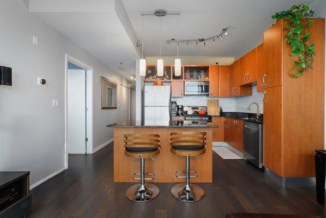 kitchen with appliances with stainless steel finishes, a kitchen island, decorative light fixtures, backsplash, and a breakfast bar