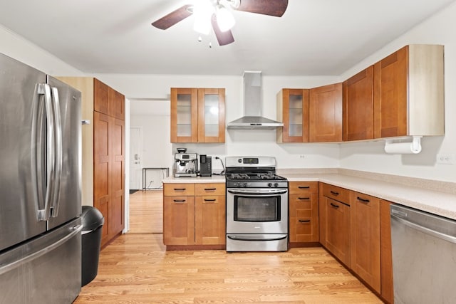 kitchen with ceiling fan, light hardwood / wood-style flooring, wall chimney exhaust hood, and appliances with stainless steel finishes