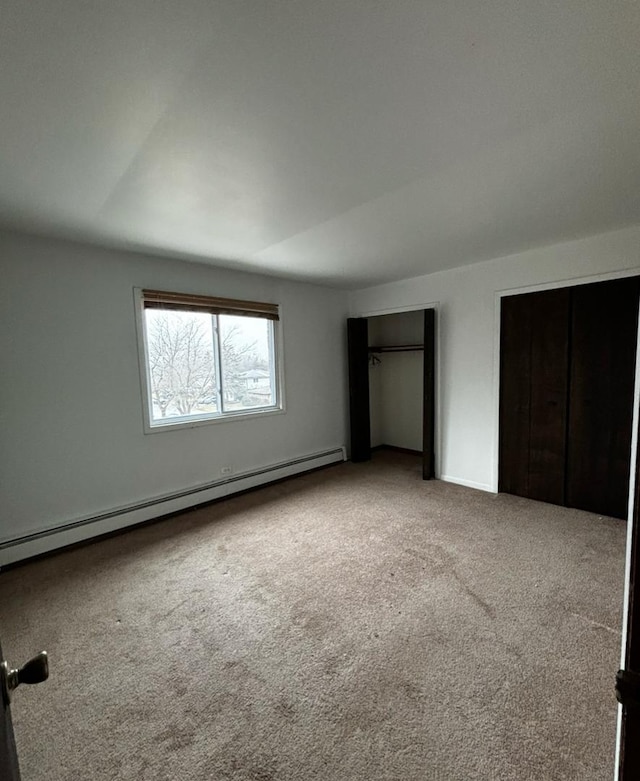 unfurnished bedroom featuring a baseboard radiator, multiple closets, and carpet