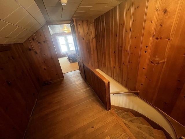 hall with light hardwood / wood-style floors, wood walls, and lofted ceiling