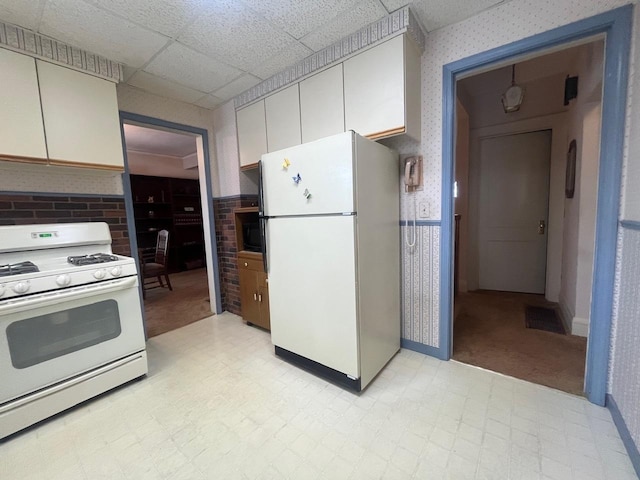 kitchen with a paneled ceiling, white cabinets, and white appliances