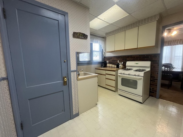 kitchen with a paneled ceiling, cream cabinets, white gas stove, and sink