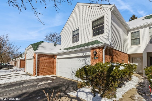 snow covered property with a garage, aphalt driveway, and brick siding