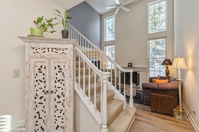 staircase with baseboards, radiator, a high ceiling, wood finished floors, and a ceiling fan