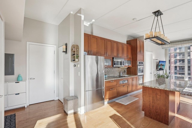 kitchen featuring stone counters, light wood-type flooring, appliances with stainless steel finishes, tasteful backsplash, and decorative light fixtures