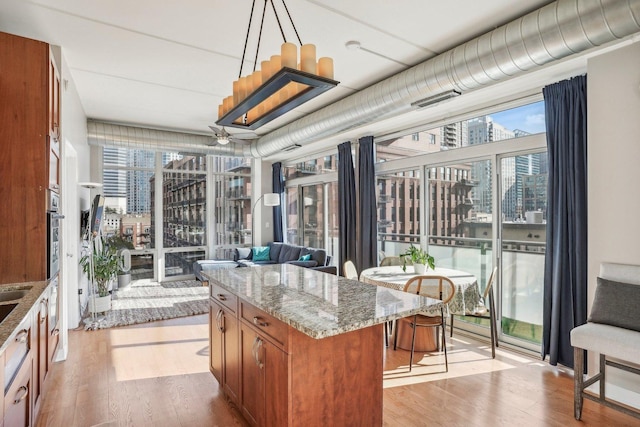 kitchen featuring a center island, hanging light fixtures, light stone counters, light hardwood / wood-style floors, and a breakfast bar area