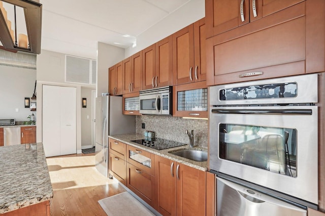 kitchen featuring sink, light hardwood / wood-style flooring, decorative backsplash, light stone counters, and stainless steel appliances